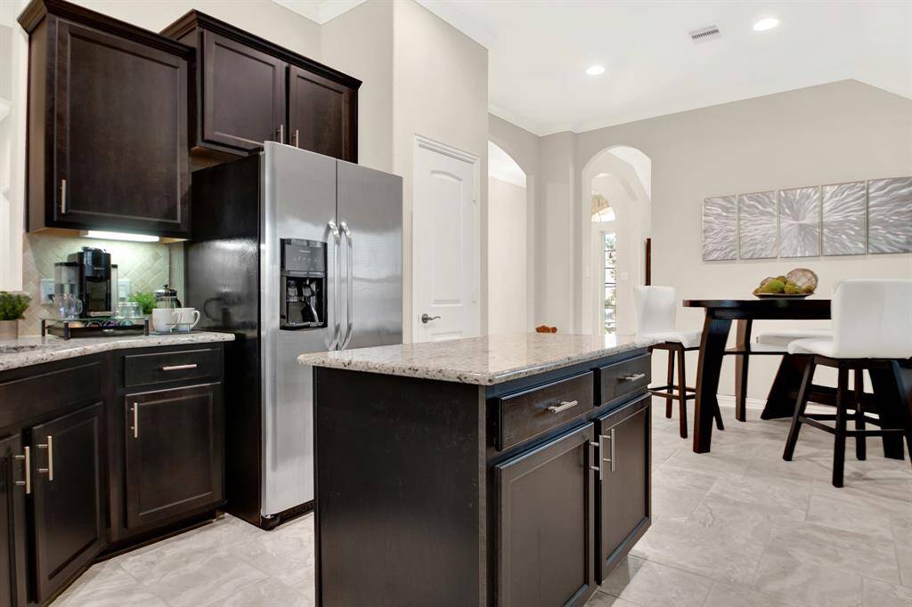 This modern kitchen features dark cabinetry, stainless steel appliances, and sleek granite countertops. It opens into a bright dining area with stylish decor and tile flooring, providing a welcoming space for gatherings.