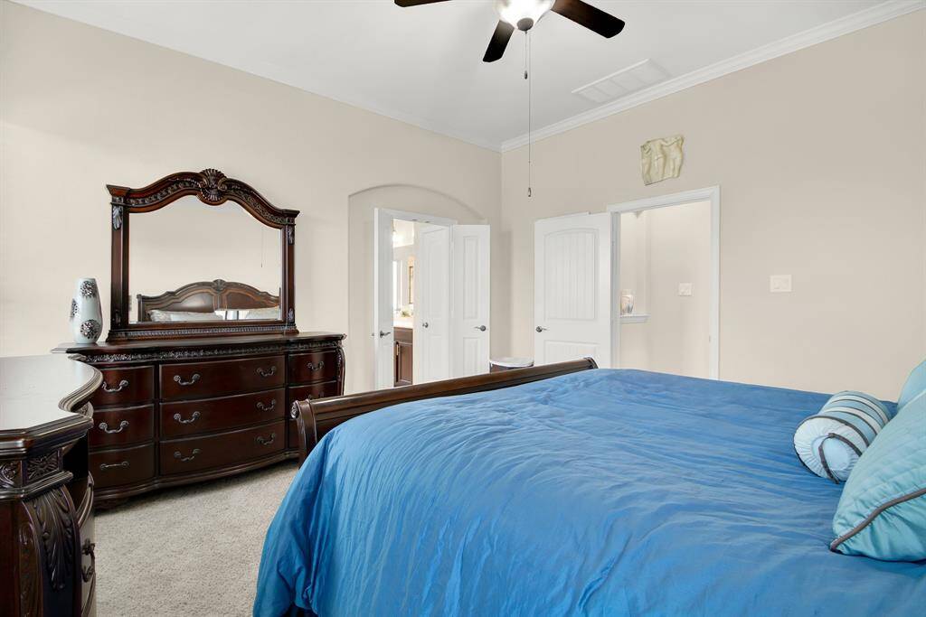 This photo showcases a spacious bedroom with elegant dark wood furniture, including a dresser with a mirror. The room features a ceiling fan, light walls, and plush carpeting, offering a cozy and inviting atmosphere.