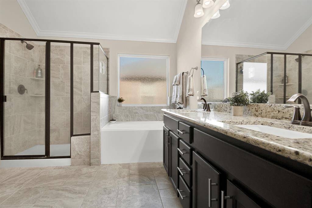 This bathroom features a modern design with a spacious walk-in shower, a separate soaking tub, and a dual-sink vanity with granite countertops. Neutral tile flooring and ample natural light create a bright and inviting atmosphere.