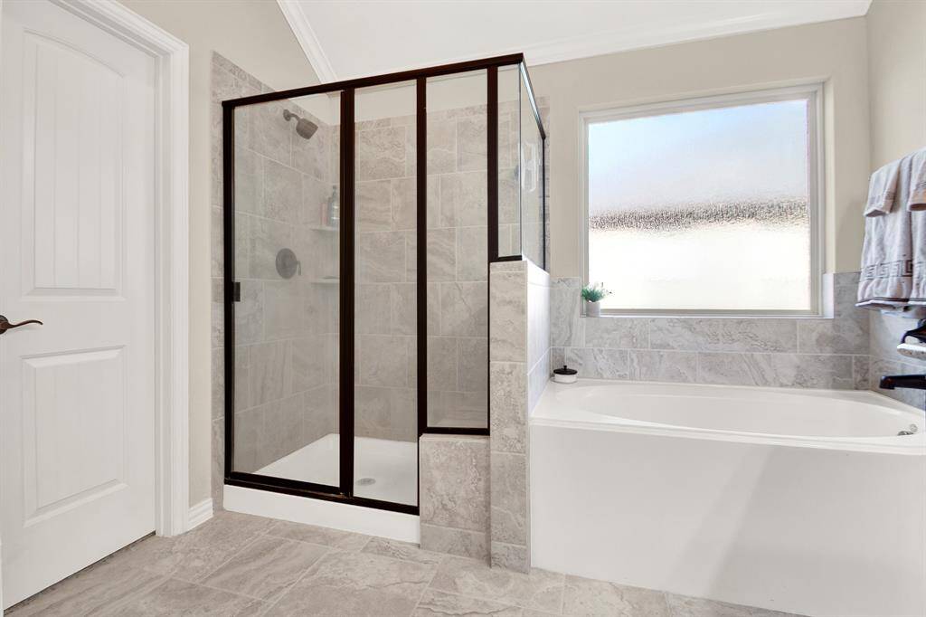 This bathroom features a modern design with a glass-enclosed shower and a separate bathtub. It has elegant tile work and a large frosted window for natural light and privacy.