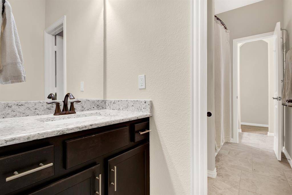 This photo shows a modern bathroom with a granite countertop, dark wood cabinets, and a sleek faucet. There's a shower with a curtain in the background and tile flooring, creating a clean and inviting space.