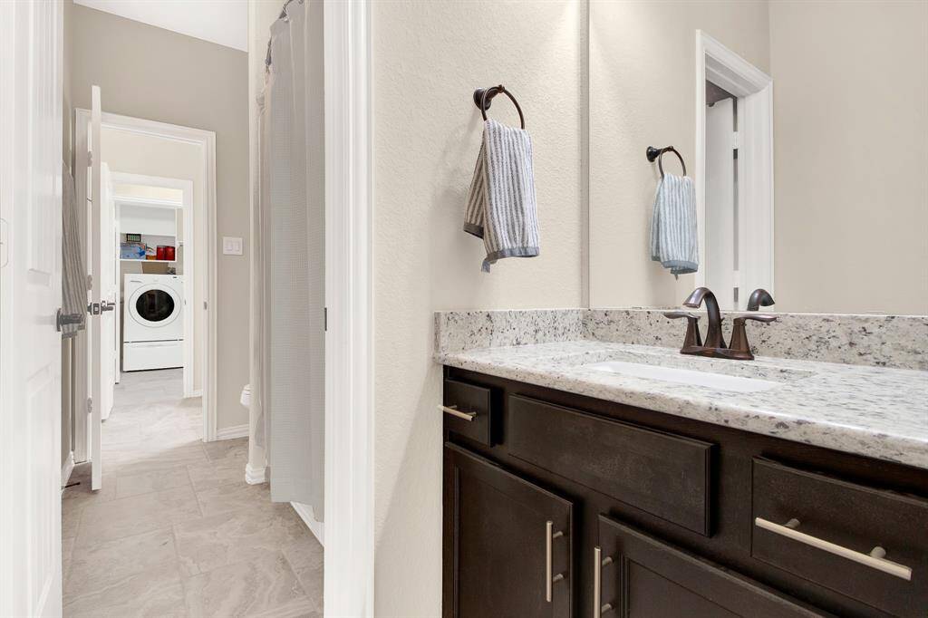 This photo shows a modern bathroom with a granite countertop and dark wood cabinetry. There's a view into a laundry room with a washer and dryer, showcasing the home's convenient layout.