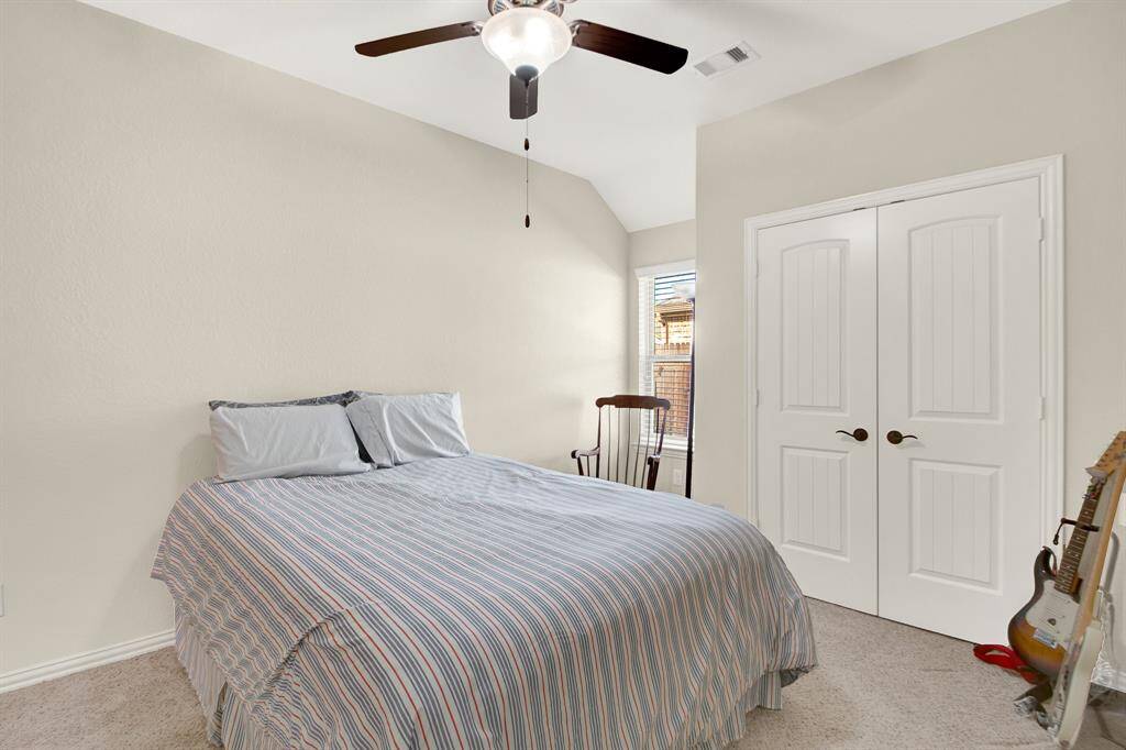 This cozy bedroom features neutral walls, a ceiling fan, and a double-door closet. Natural light streams through the window, enhancing the inviting atmosphere.