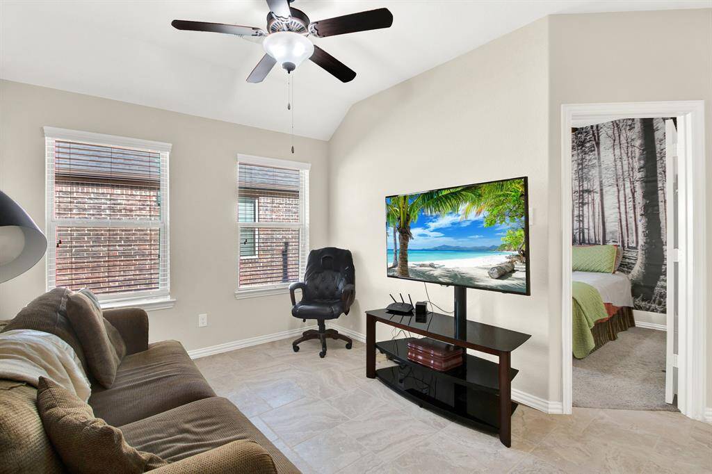 This cozy room features a ceiling fan, two large windows for natural light, a comfortable couch, and a TV setup. It opens into a bedroom with a scenic wall mural, offering a relaxing atmosphere.