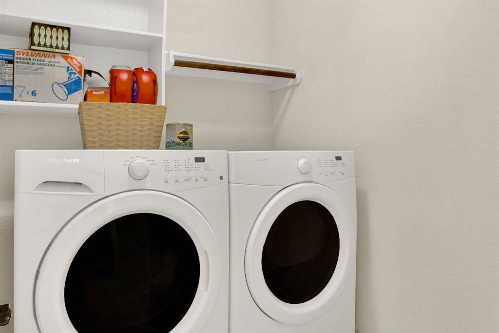 This photo shows a compact laundry room with a Frigidaire washer and dryer set, white walls, open shelving for storage, and a small selection of laundry supplies.