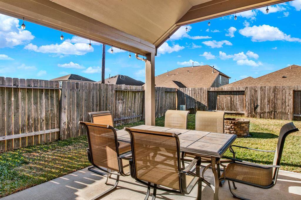 This photo showcases a cozy backyard patio with a covered seating area, string lights, and a fenced lawn, perfect for outdoor dining and relaxation.