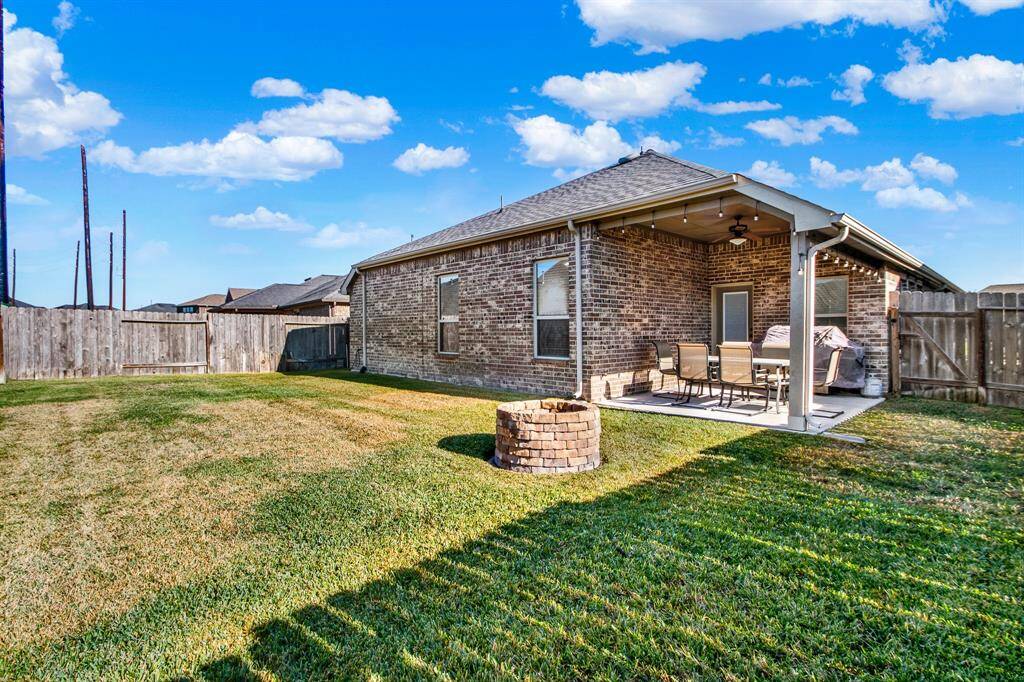 Spacious backyard with a covered patio perfect for outdoor dining, a brick fire pit for cozy gatherings, and well-maintained lawn, all enclosed by a wooden fence.