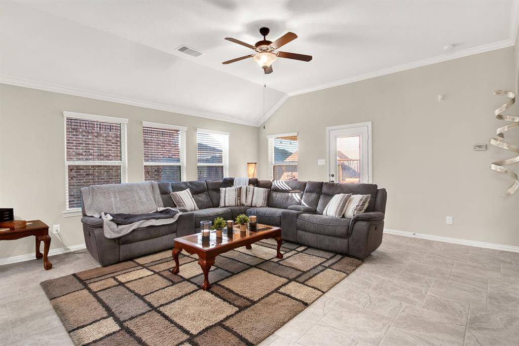 Bright and welcoming living room with neutral tones, featuring a large sectional sofa, ceiling fan, and ample natural light from multiple windows. The space is complemented by a cozy area rug and a stylish coffee table.