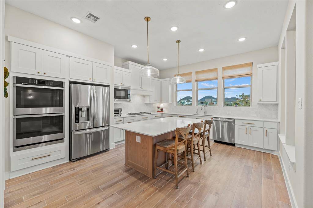 Features include silestone countertops paired with a coordinating tile backsplash, stainless steel appliances, crisp white cabinets with updated hardware, under cabinet lighting, recessed lighting, pendant lighting and a sprawling island with breakfast bar seating.