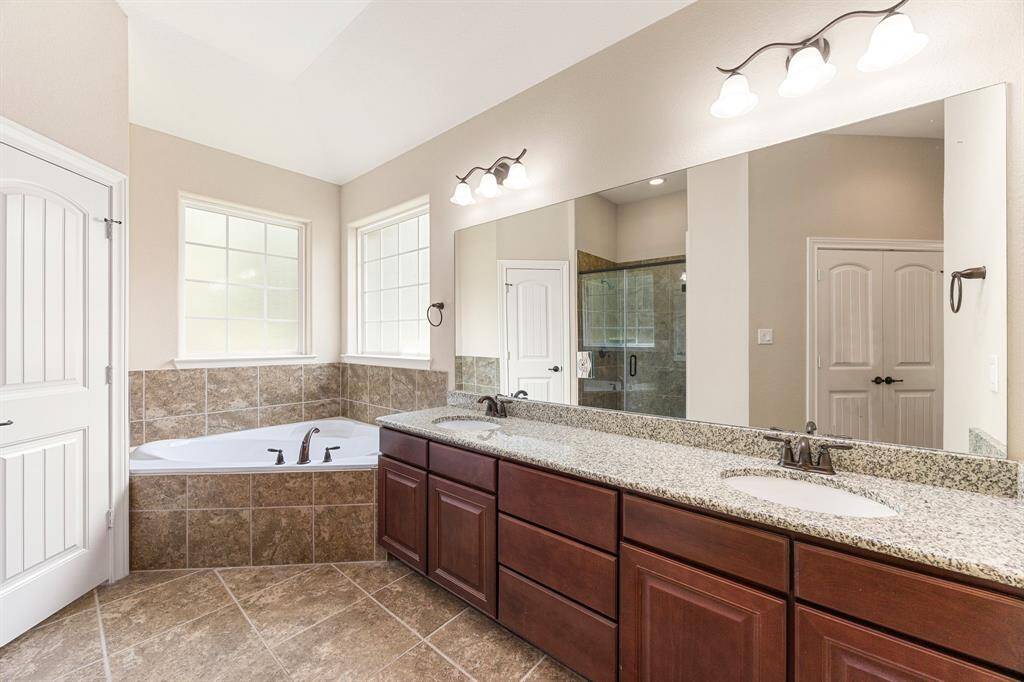 This primary bathroom is definitely move-in ready! Featuring a dark framed walk-in shower with tile surround, separate garden tub for soaking after a long day with custom tile detailing, dark stained cabinets with light countertops, spacious walk-in closet with shelving, high ceilings, custom paint, sleek and dark modern finishes.
