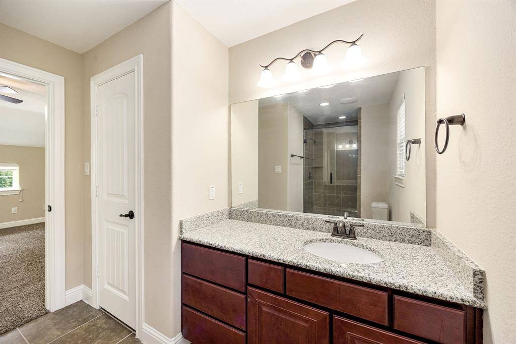 Secondary bath features tile flooring, bath/shower combo with tile surround, dark wood cabinets, beautiful light countertops, mirror, dark, sleek fixtures and modern finishes.