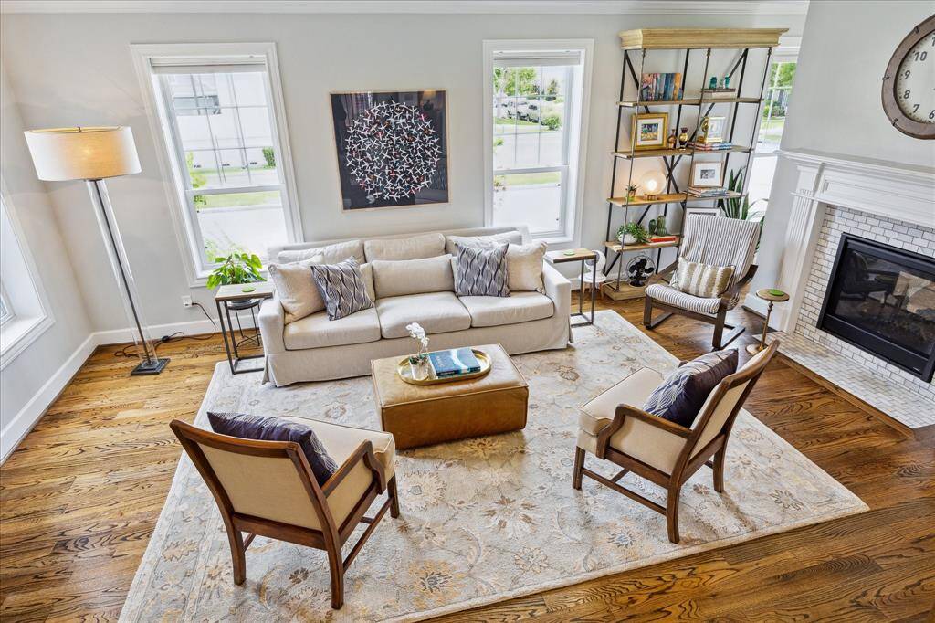 Bathed in natural light, this expansive living room showcases warm hardwood floors, elegant trim details, and a cozy fireplace, all anchored by refined furnishings and a serene, welcoming aesthetic.