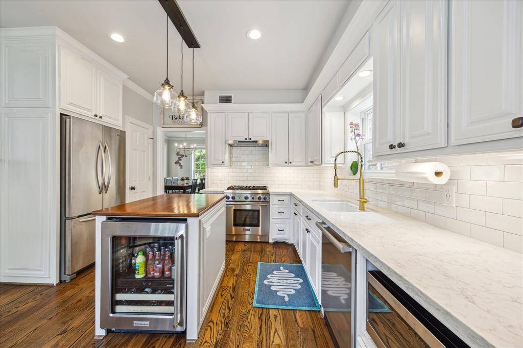 This gourmet kitchen exudes style and function with sleek quartz countertops, professional-grade stainless appliances, a butcher block island with beverage fridge, and a statement brass faucet beneath a bright garden window.