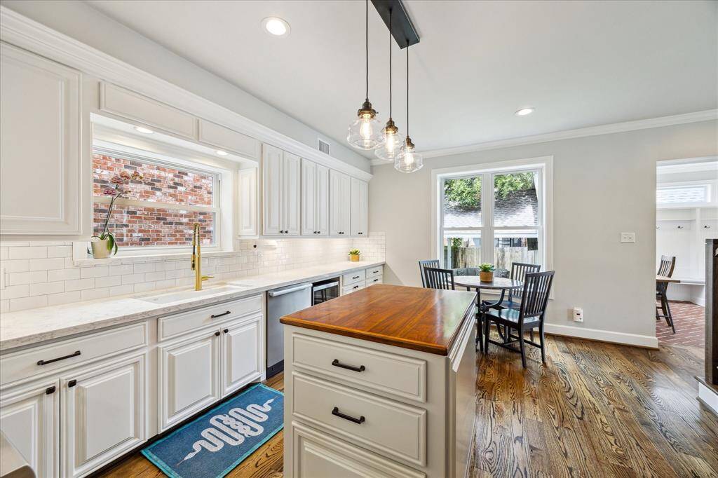 An additional view of the kitchen highlights the expansive marble-look countertops, crisp white cabinetry, warm butcher block island, and sunlit breakfast nook framed by oversized picture windows.
