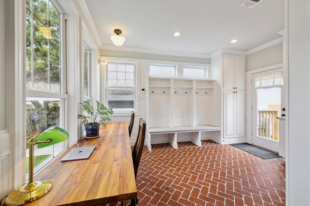This light-filled mudroom and workspace combination features charming herringbone brick flooring, a custom built-in bench with storage, and a sleek wood-topped desk overlooking the backyard through a wall of windows.