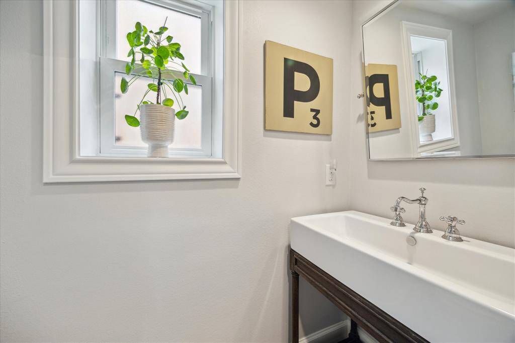 This charming powder bath features a sleek trough-style sink with polished chrome fixtures, contemporary wall art, and a frosted window that fills the space with soft natural light.