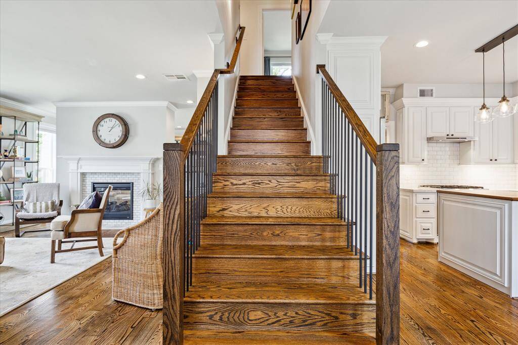 A striking central staircase with rich hardwood treads and sleek iron balusters elegantly connects the open-concept main living area to the upper level, framed by views of the stylish kitchen and inviting fireplace.
