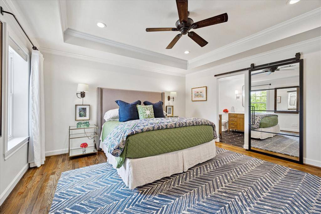 The serene primary suite offers a peaceful retreat with a tray ceiling, rich hardwood floors, and a stylish barn door leading to the spa-inspired en-suite bath.