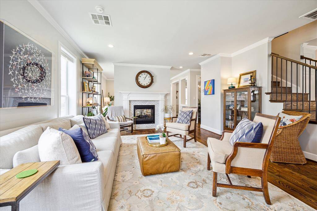 This inviting living room exudes warmth and sophistication with its rich hardwood floors, elegant fireplace, and abundant natural light accentuating the stylish, comfortable furnishings.