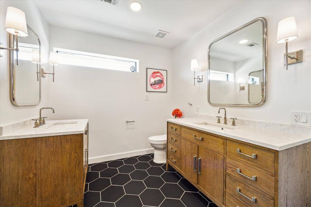 The primary bath exudes modern sophistication with dual wood vanities topped in marble, striking black hex tile flooring, and designer lighting that enhances the spa-like ambiance.