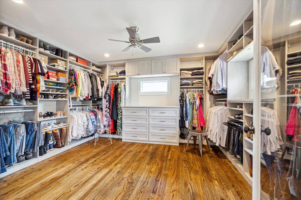 The expansive primary walk-in closet is a dream, featuring custom built-ins, abundant hanging space, soft-close drawers, and elegant hardwood floors under recessed lighting.