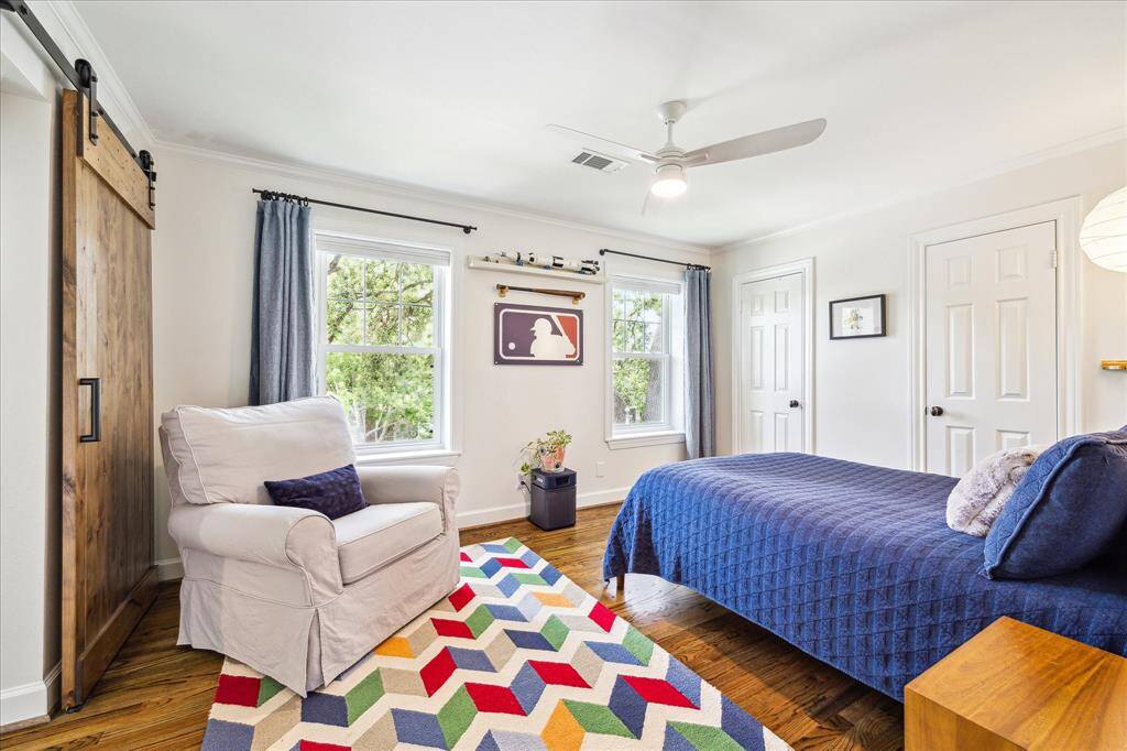 This cheerful secondary bedroom features rich hardwood floors, dual closets, abundant natural light, and a rustic sliding barn door that adds a touch of character and charm.