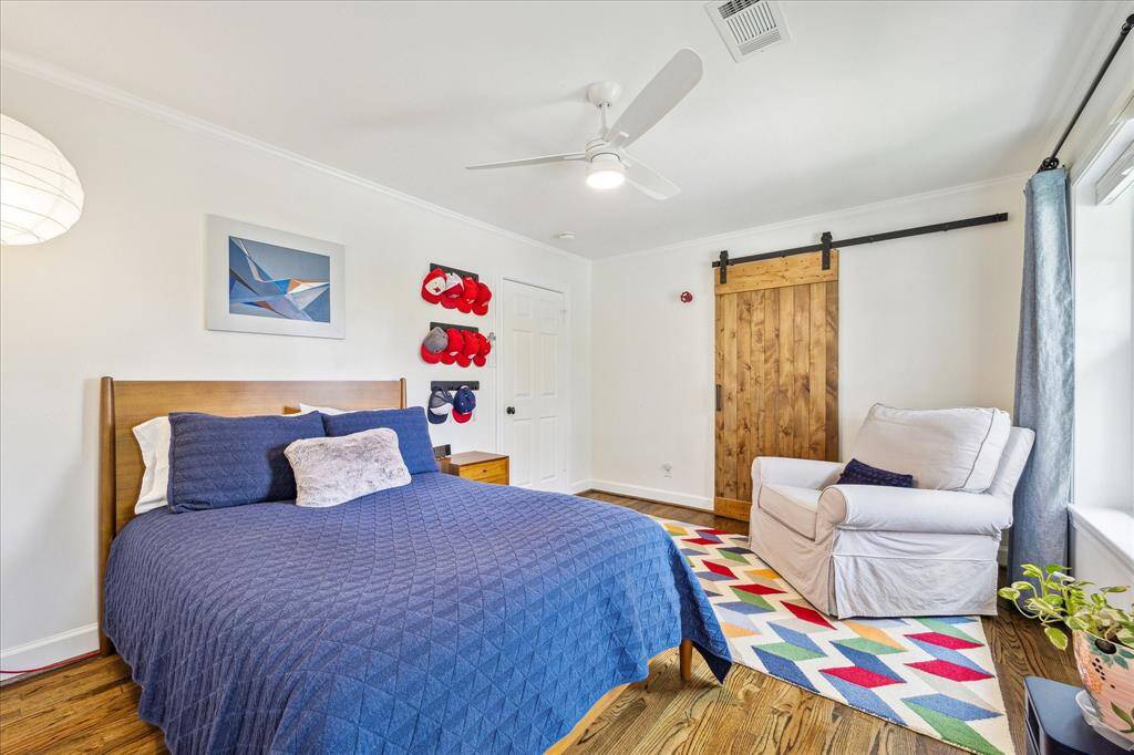 An additional view of the secondary bedroom reveals a bright and playful space with a modern ceiling fan, cozy reading nook, and colorful accents that complement the rustic barn door and warm hardwood floors.