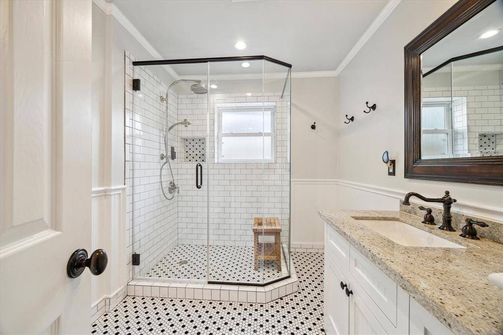 This beautifully appointed secondary bathroom features timeless black and white tile, a spacious glass-enclosed shower with designer inlay, and a granite-topped vanity with oil-rubbed bronze fixtures.