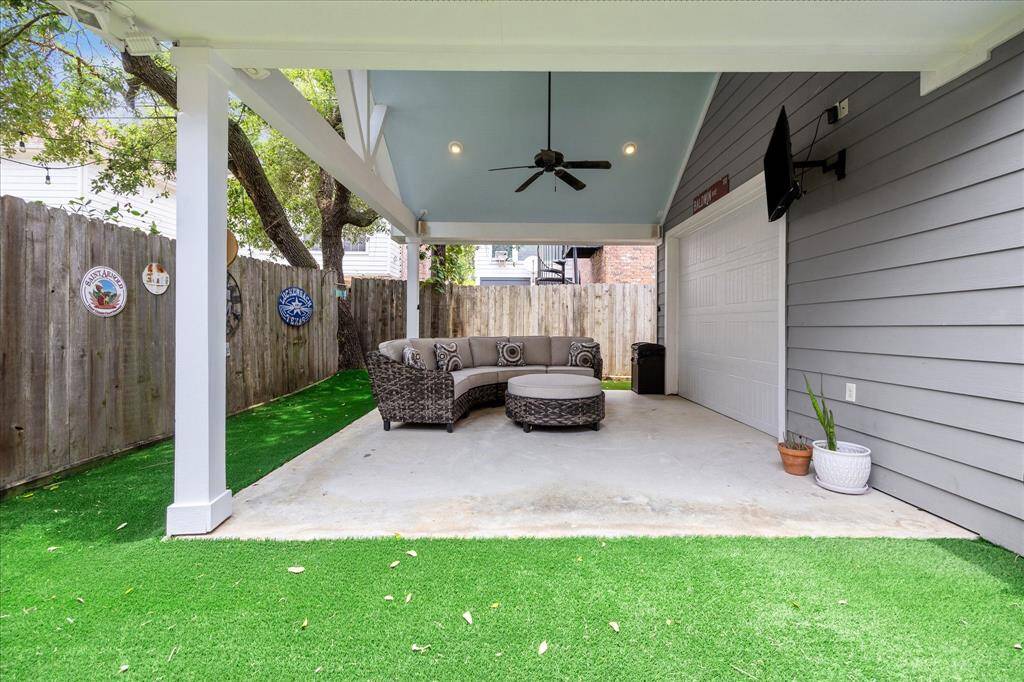 This inviting covered patio is perfect for outdoor entertaining, featuring a vaulted ceiling with recessed lighting and fan, a mounted TV, and low-maintenance turf for year-round greenery.