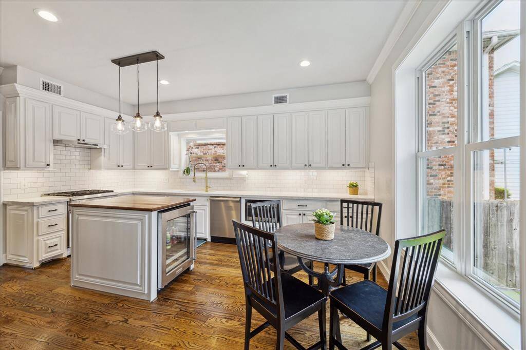 This bright and beautifully updated kitchen features custom white cabinetry, a butcher block island with built-in beverage fridge, designer pendant lighting, and a charming breakfast nook overlooking the backyard through expansive windows.