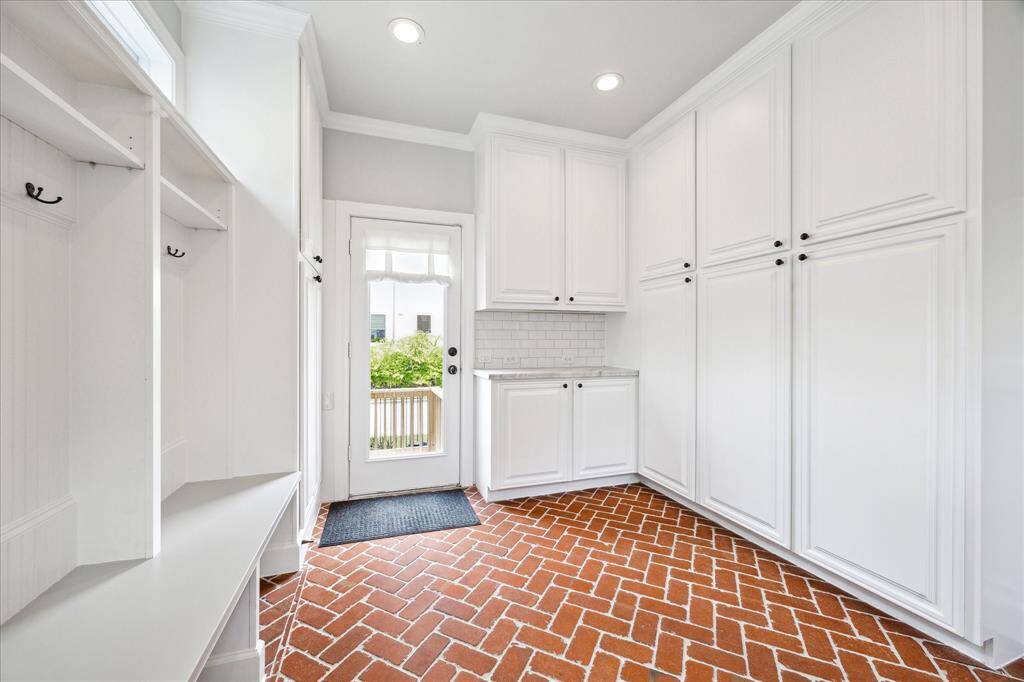 This stylish mudroom showcases timeless brick herringbone flooring, abundant custom cabinetry, and built-in storage benches, all seamlessly blending functionality with elegant design.