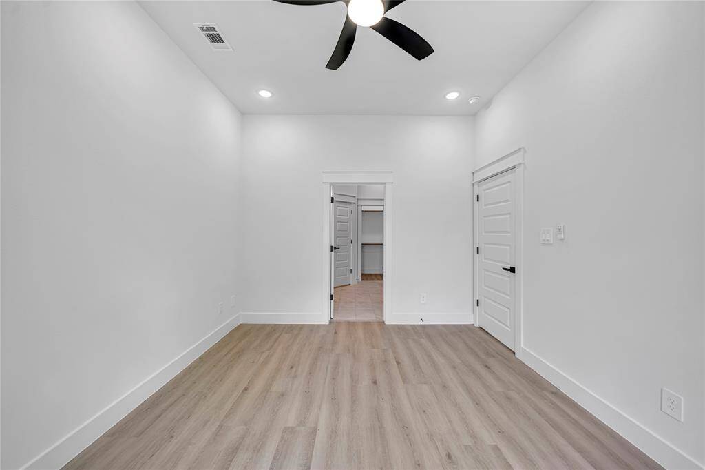 Bright master bedroom with large window, modern ceiling fan, recessed lighting, and light wood flooring.