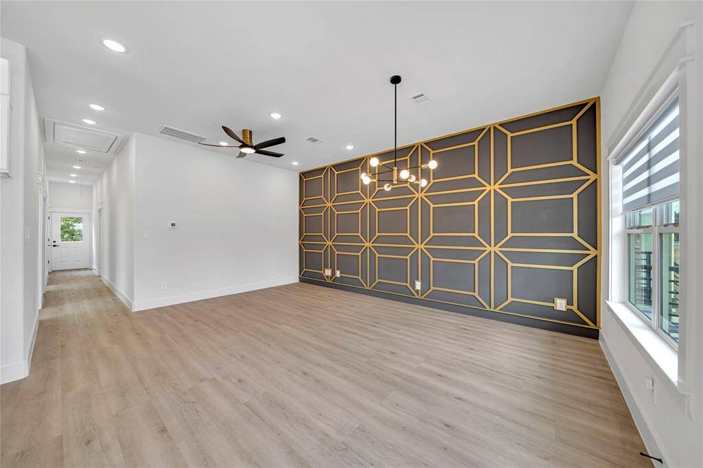 Open-concept living space features a stylish geometric accent wall, light wood flooring, and contemporary lighting fixtures