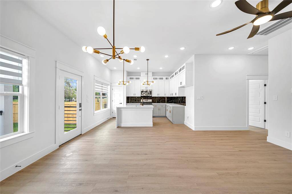 Living area features stylish wood flooring and ample natural light. The kitchen boasts a sleek island with contemporary lighting fixtures, perfect for entertaining.