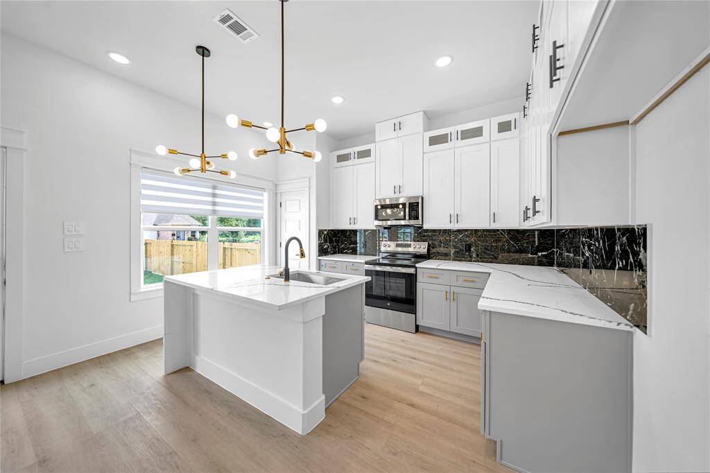 This kitchen features sleek white cabinetry, a striking marble island with a built-in sink. Stainless steel appliances and wood flooring, while ample natural light enhances the space.
