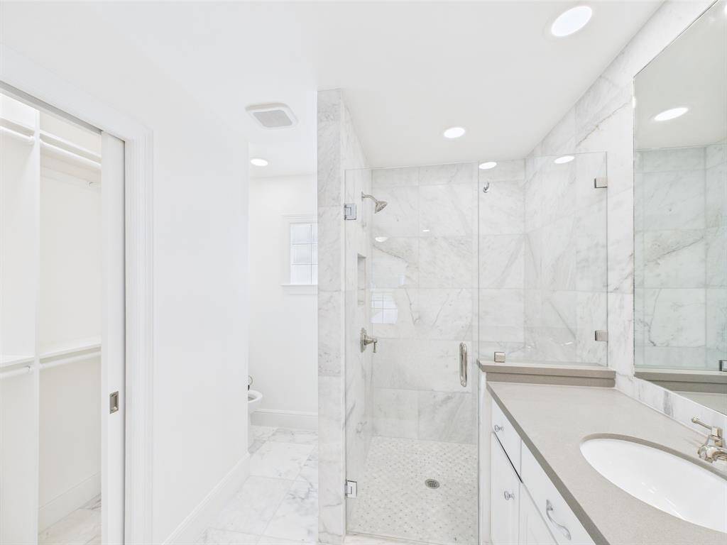 Primary bathroom features a sleek, modern design with marble tiles, a spacious glass-enclosed shower, and a single-sink vanity. It also includes a walk-in closet, enhancing functionality and storage.