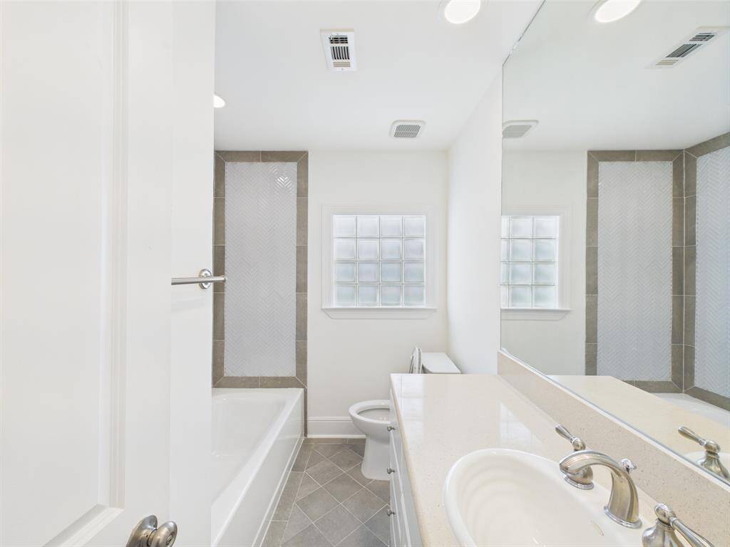 The secondary bathroom features a clean, modern design with a bathtub and shower area, a large mirror, stylish fixtures, and ample natural light from a glass block window.