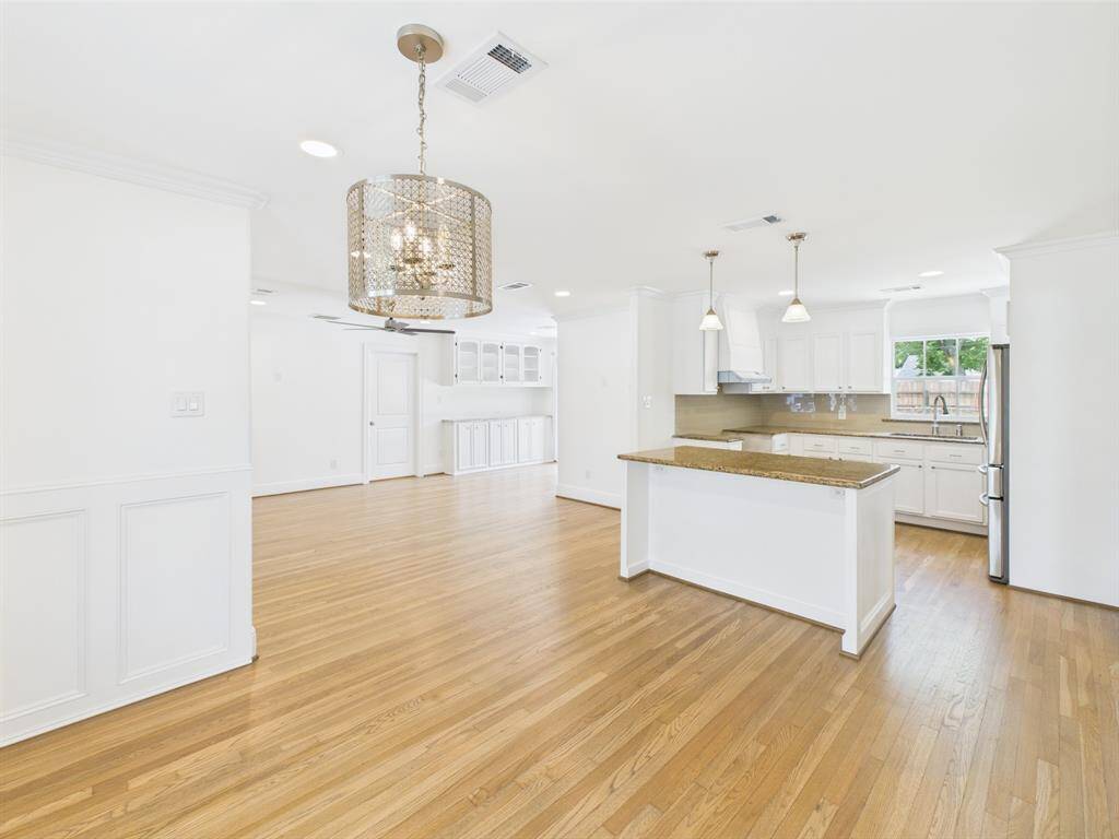 Open-concept space features hardwood floors and a bright, airy kitchen with white cabinetry, granite countertops, and modern pendant lighting. The dining area includes a stylish chandelier, creating a welcoming atmosphere.