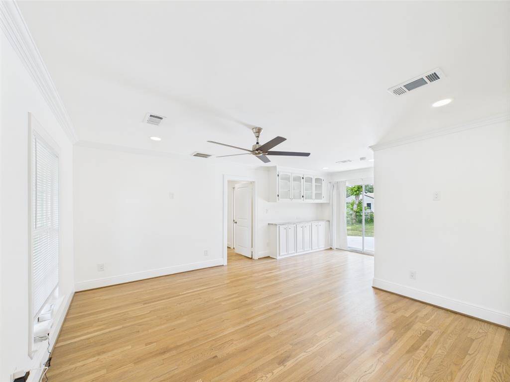 Bright, open living space with hardwood floors, ceiling fan, and built-in cabinetry. Large windows and sliding glass door offer plenty of natural light and access to the backyard.