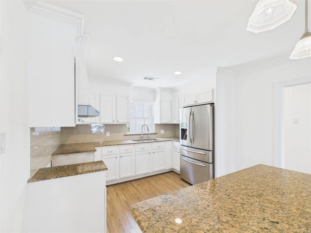 This bright, modern kitchen features white cabinetry, granite countertops, stainless steel appliances, and wood flooring, offering a clean and inviting space. New Oven will be added soon!