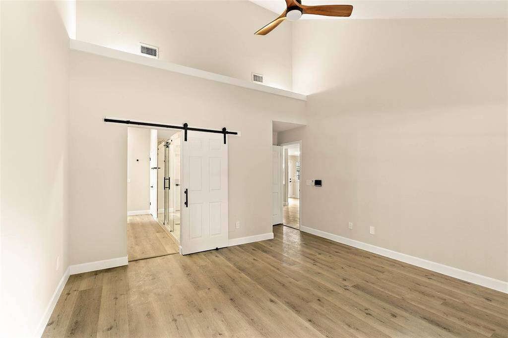 Beautifully updated primary bedroom features high ceilings and a modern white barn door that adds a touch of character to the airy space.