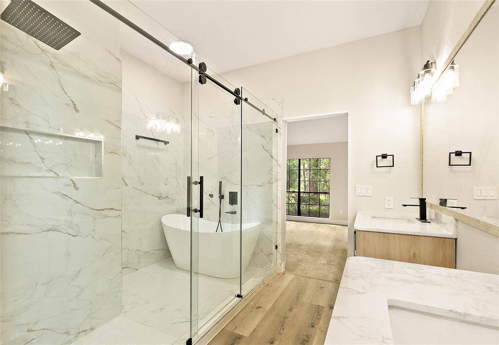 Spa-like ensuite featuring a large marble-look tiled walk-in shower and freestanding soaking tub. Double vanity with modern wood cabinetry and quartz counters. Enjoy serene views from the large window.