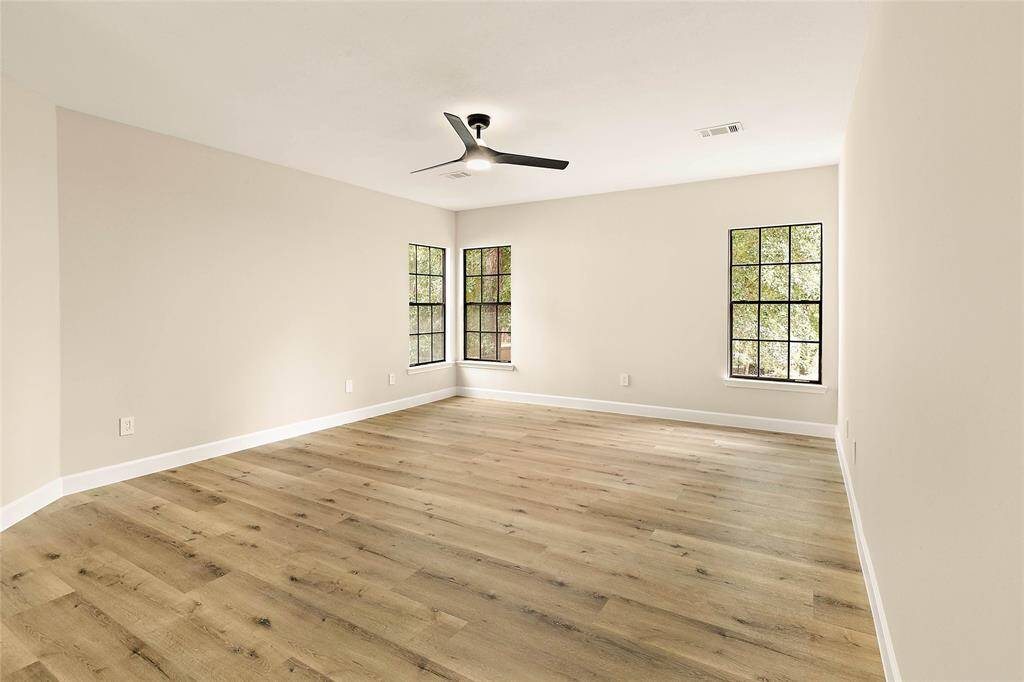 Generous secondary bedroom bathed in natural light from multiple windows. Features contemporary wood-look flooring and a sleek ceiling fan for year-round comfort. A versatile space ready for personalization.