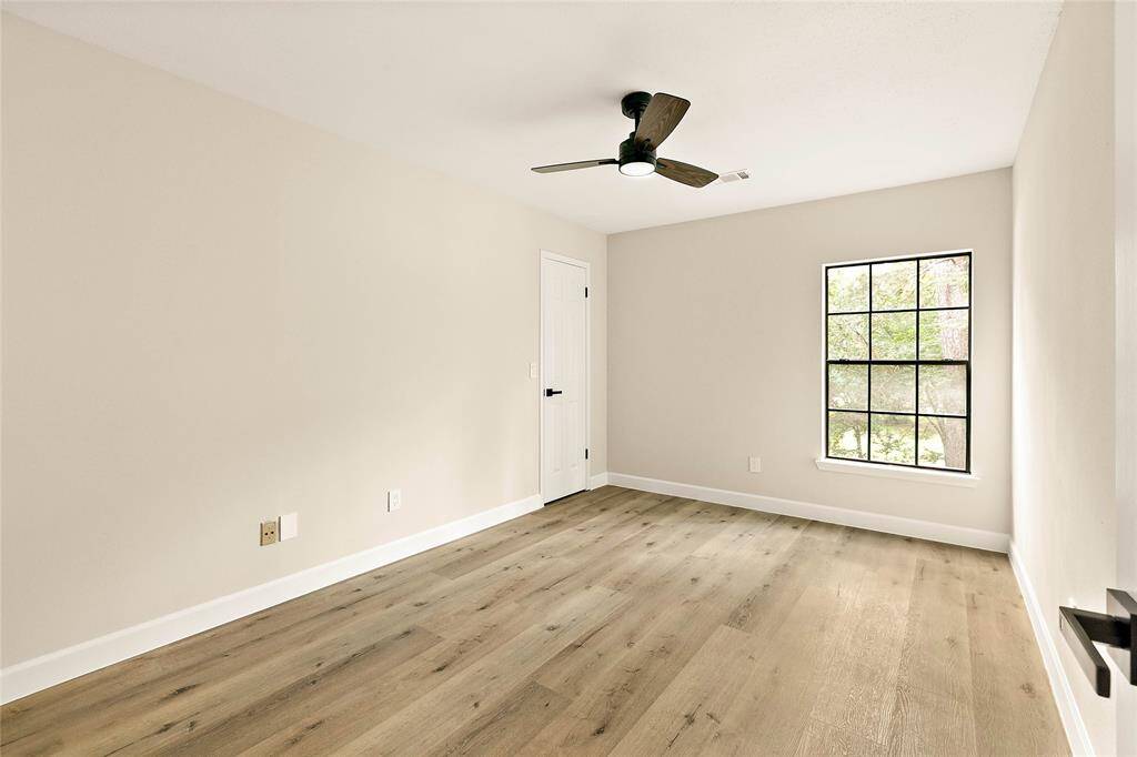Another inviting bedroom featuring contemporary wood-look flooring and a clean aesthetic. Equipped with a modern ceiling fan for comfort, this space offers versatility and natural light from its well-sized window.