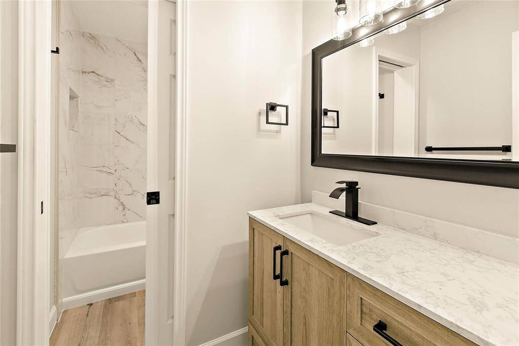 This updated bathroom showcases a light wood vanity with a quartz countertop and striking matte black fixtures. The shower area continues the clean look with coordinating marble-look tile.