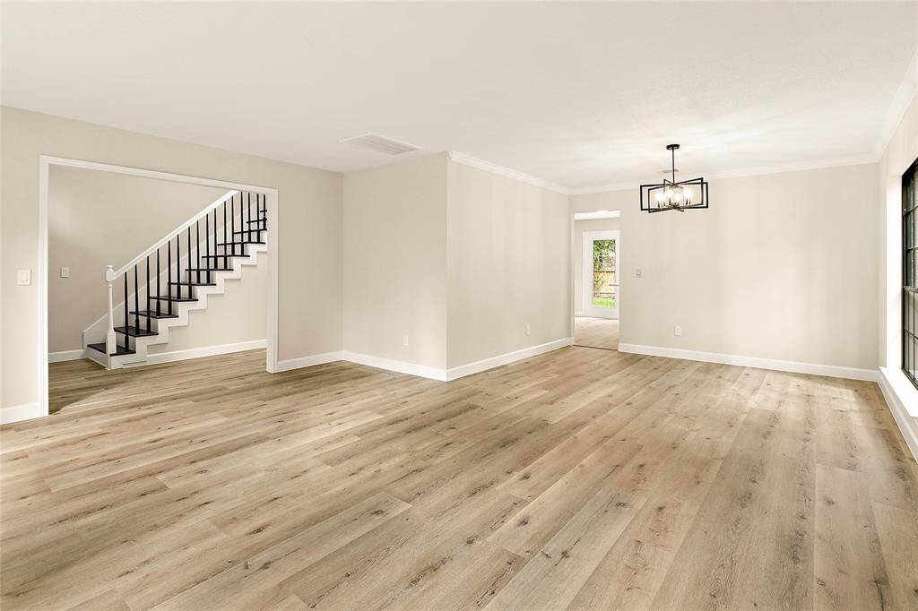 Expansive living/dining space with fresh neutral walls accented by crown molding. A contemporary chandelier illuminates the area, with a large windows provide ample natural light.