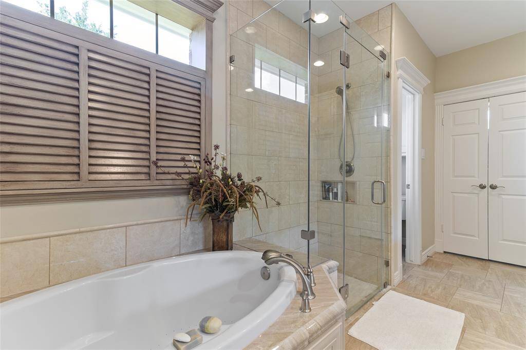 Unwind in the oversized soaking tub or refresh in the luxurious frameless glass shower, featuring floor-to-ceiling tile for a sleek, spa-inspired feel in this beautifully renovated primary bathroom.