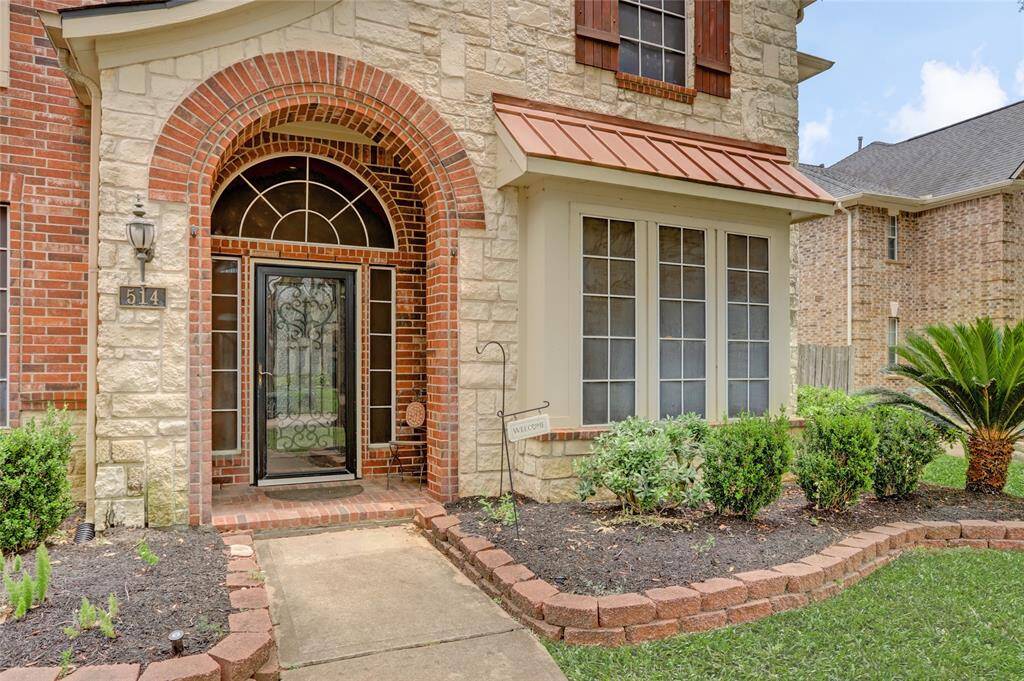 A closer look reveals a charming front entry framed by elegant stone and brick detailing and lush garden beds.