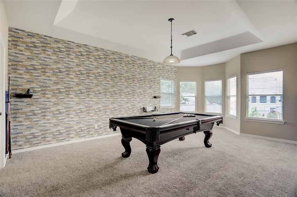 The game room features a striking brick accent wall, ample space for recreation, and large windows that fill the space with natural light.