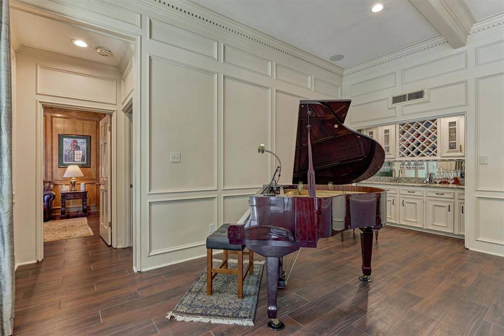 Sophisticated living room featuring a grand piano area and a built-in bar—designed for refined gatherings and timeless charm. Primary bedroom and sitting/office area off the living room.
